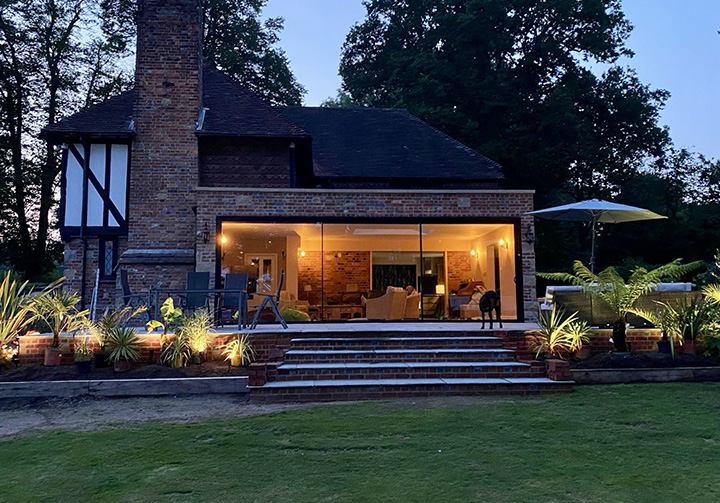house exterior with well-lit patio and garden features three steps leading to an inviting living space surrounded by greenery and a dog present