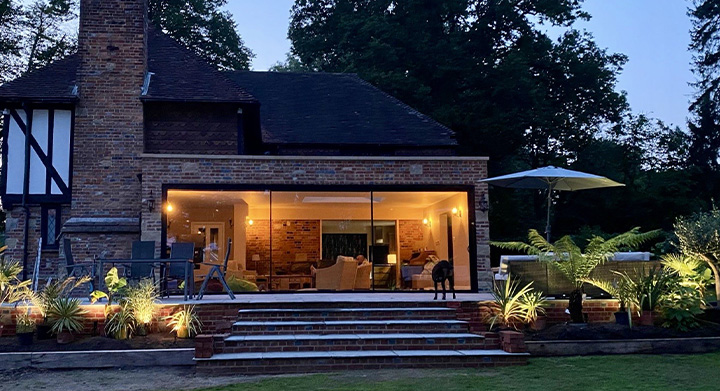 brick house with large glass patio windows surrounded by plants and garden lights at dusk two story outdoor living space